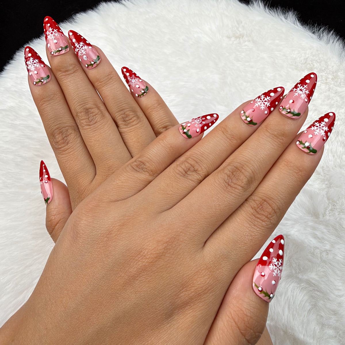 Detail shot of Holly Snow red and pink snowflake French tip Christmas almond press-on nails on hand