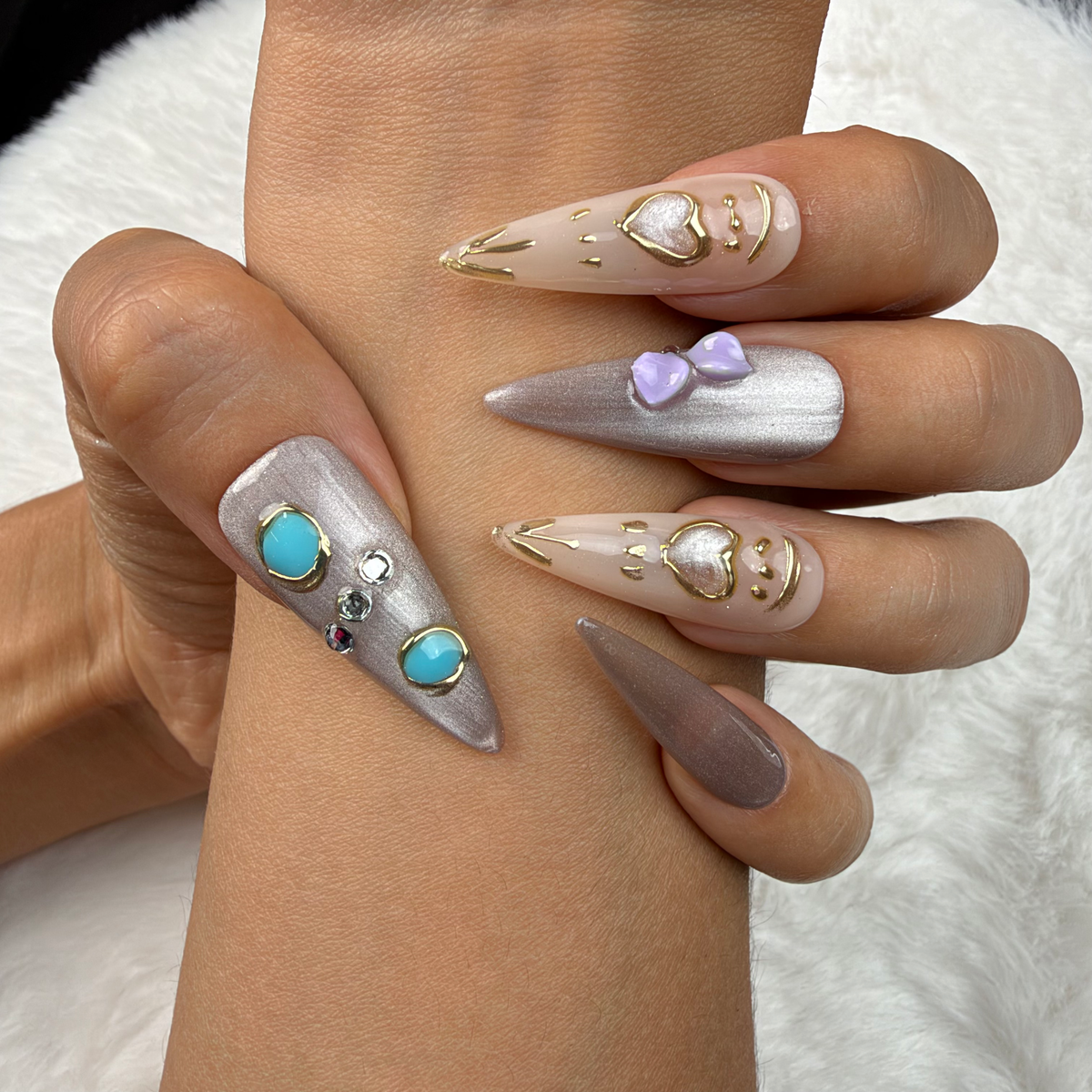 Close-up of hands wearing Silver Muse silver chrome stiletto press-on nails with turquoise stones and a heart charm