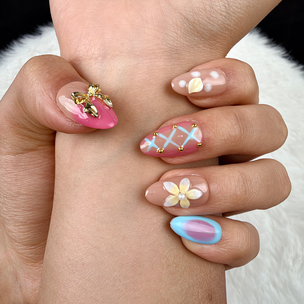 Detail shot of Sorbet Charms pink, blue and peach floral almond press-on nails with gold charms on hand