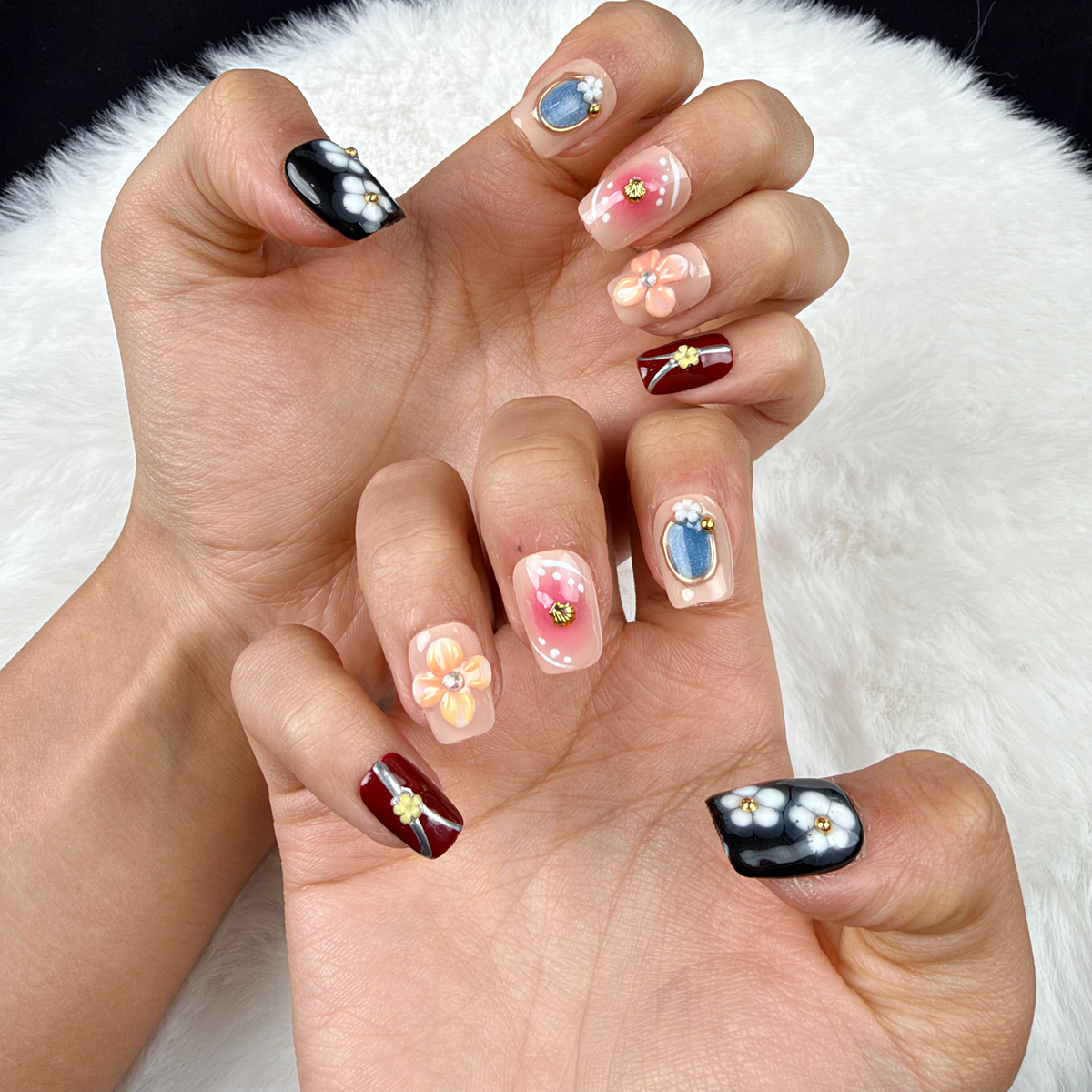 Close-up of hands wearing Blossom Mosaic nude, burgundy and black floral square press-on nails