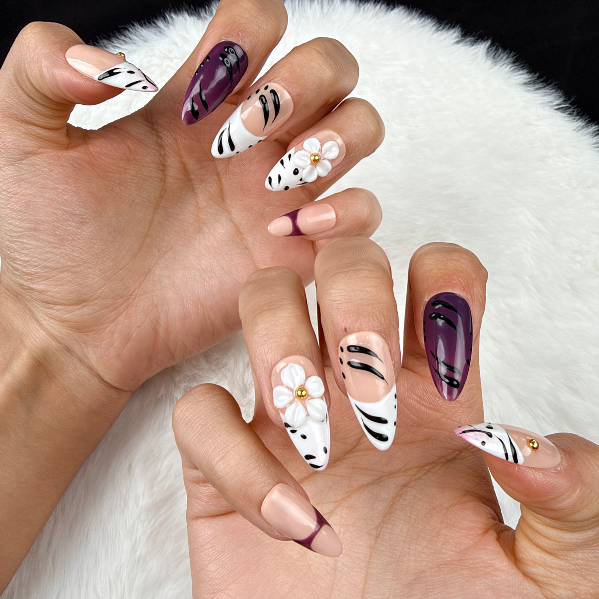 Close-up of hands wearing Plum Safari plum, black and white zebra print floral almond press-on nails