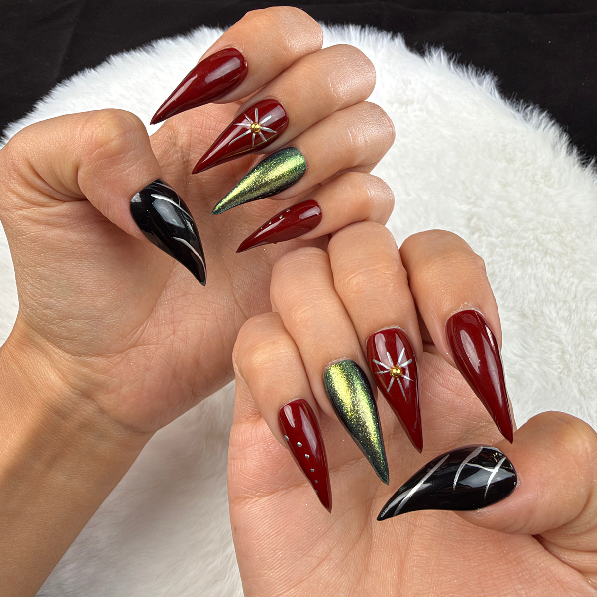 Hands wearing Ruby Orbit burgundy, green chrome and black star stiletto press-on nails