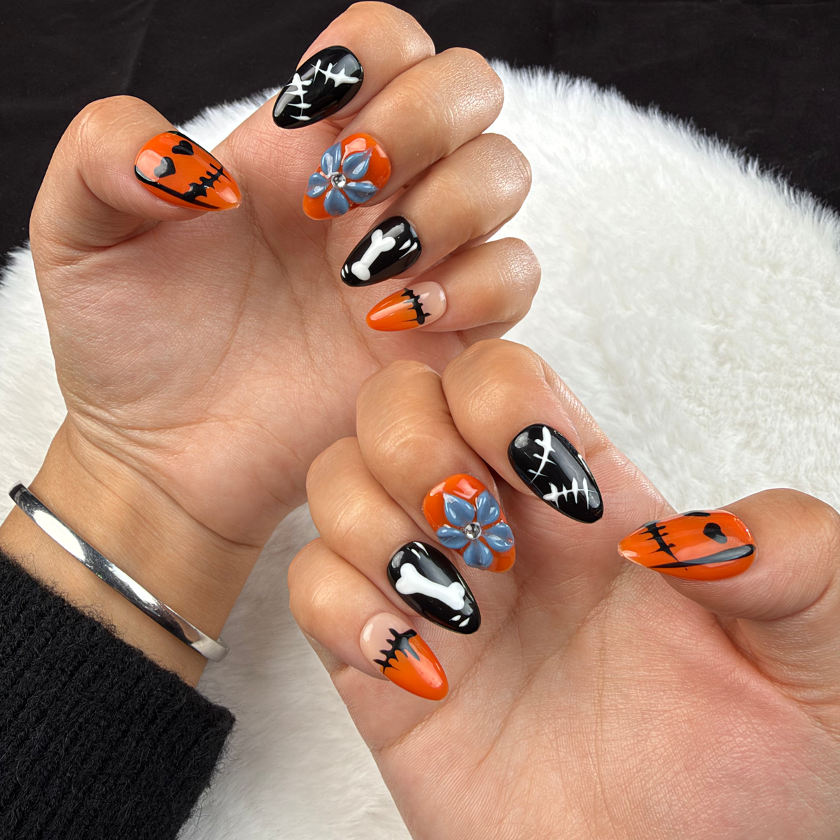 Hands wearing Spooky Petal orange and black Halloween almond press-on nails with ghosts and plaid