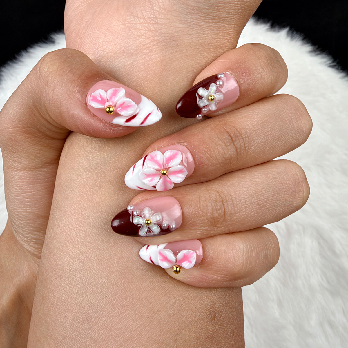 Detail shot of Rose Marble pink floral and burgundy French tip almond press-on nails on hand