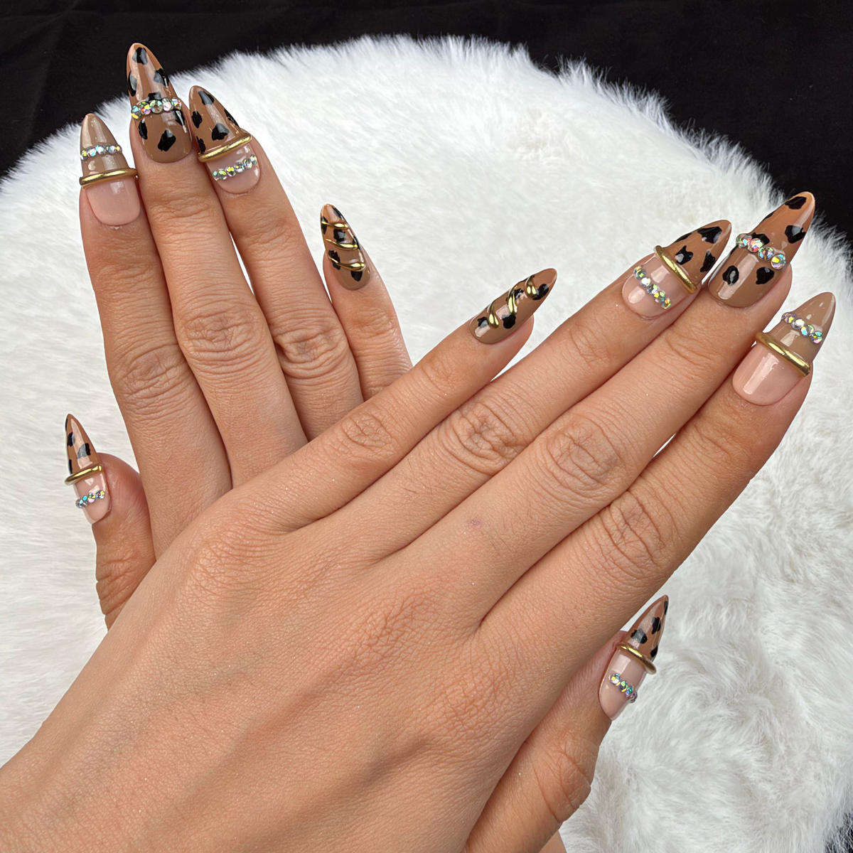 Detail shot of Wild Gleam nude leopard print almond press-on nails with gold accents and rhinestones on hand
