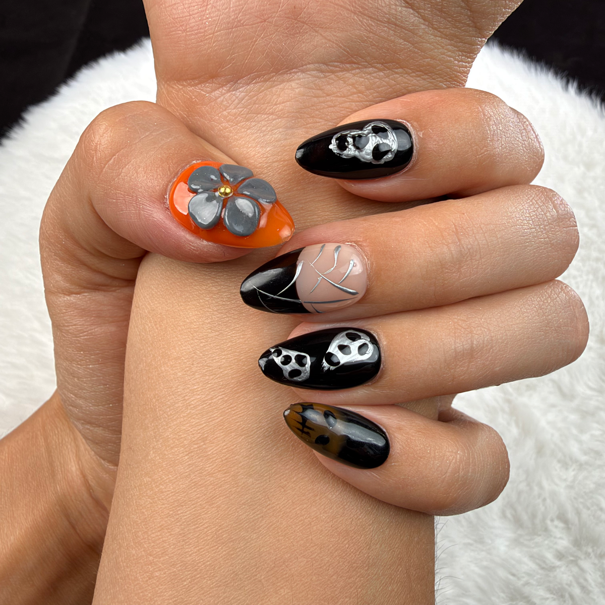 Close-up of hands wearing Midnight Web black and orange skull and spiderweb almond press-on nails