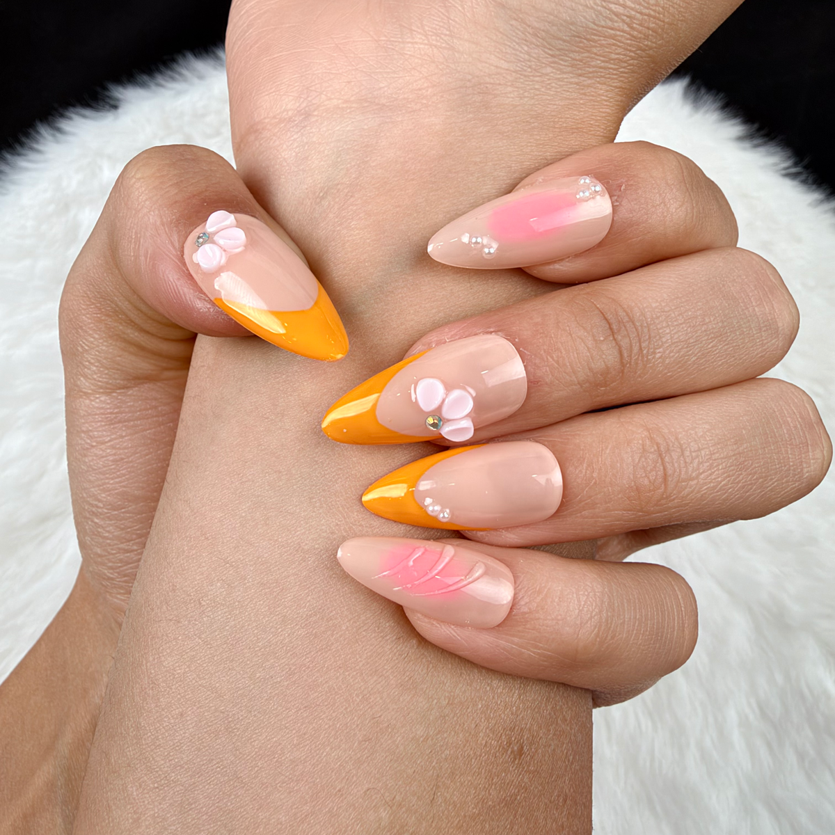 Detail shot of Apricot Petals orange French tip and pink floral almond press-on nails on hand