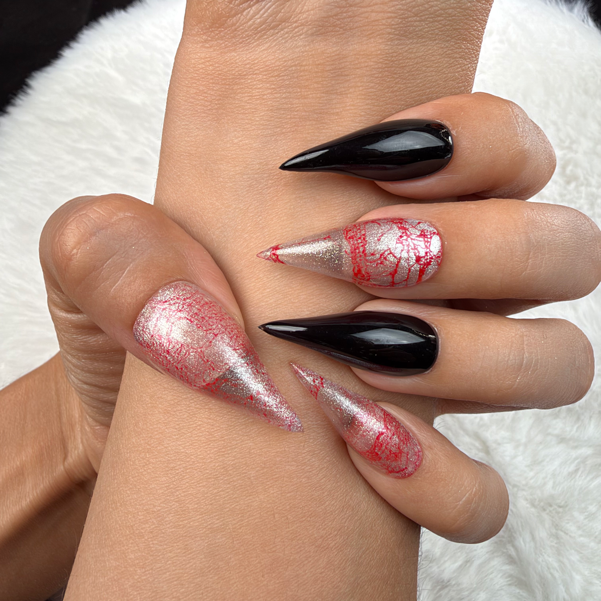 Close-up of hands wearing Rose Static pink and silver crackle and black stiletto press-on nails