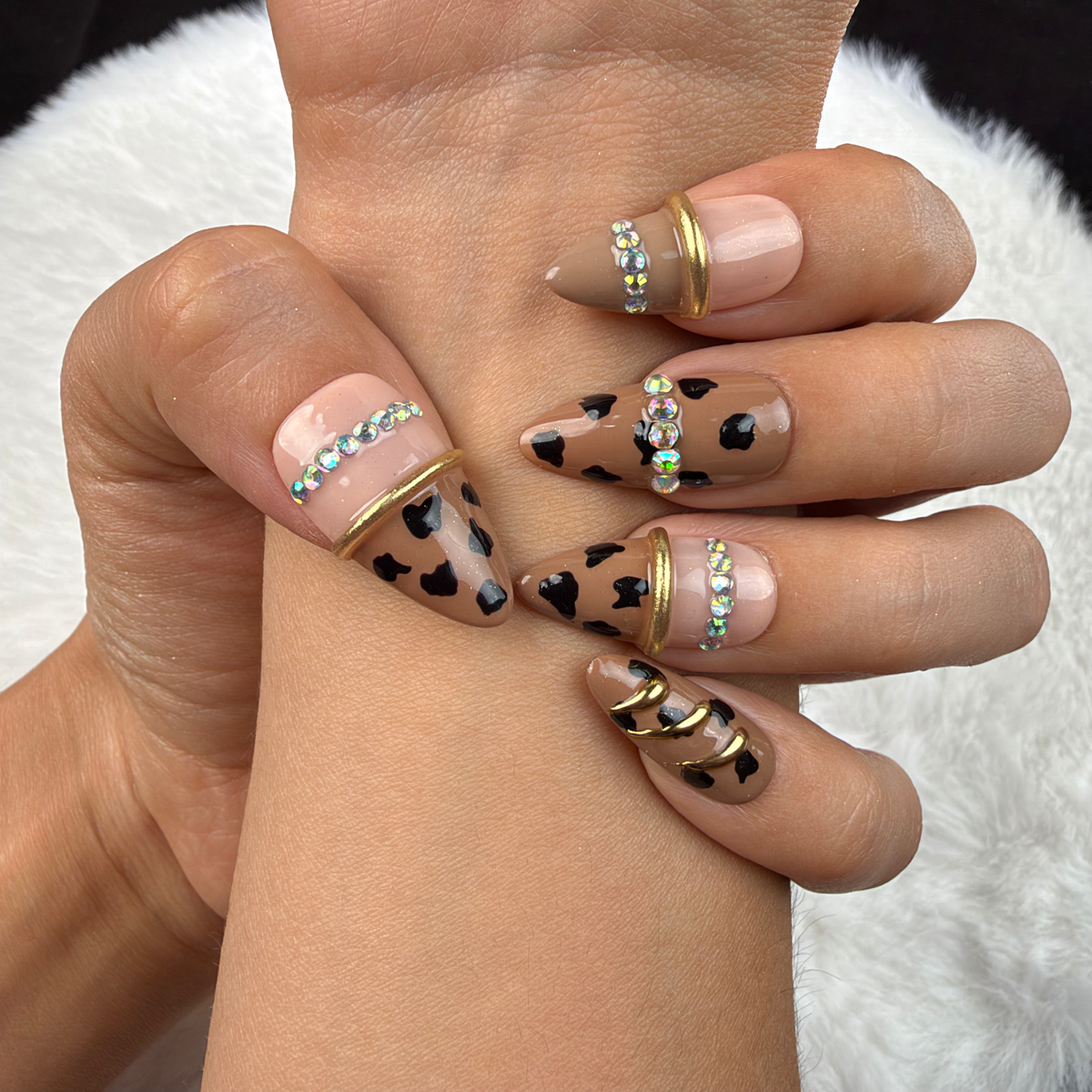 Close-up of hands wearing Wild Gleam nude leopard print almond press-on nails with gold accents and rhinestones