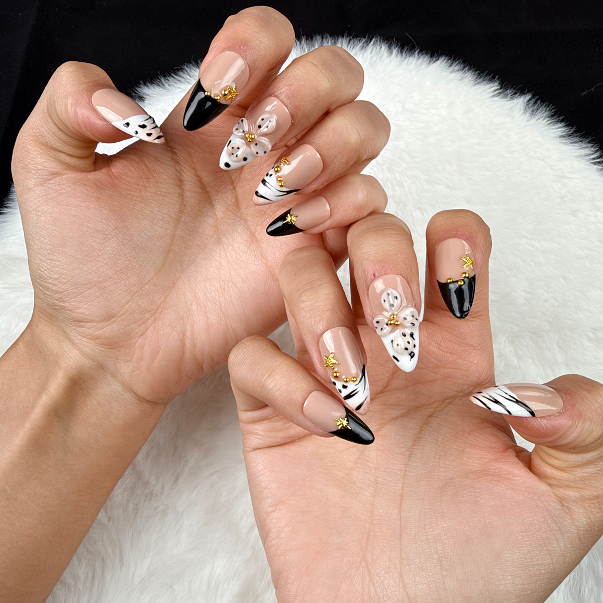 Close-up of hands wearing Golden Safari black and white zebra print French tip almond press-on nails with gold accents