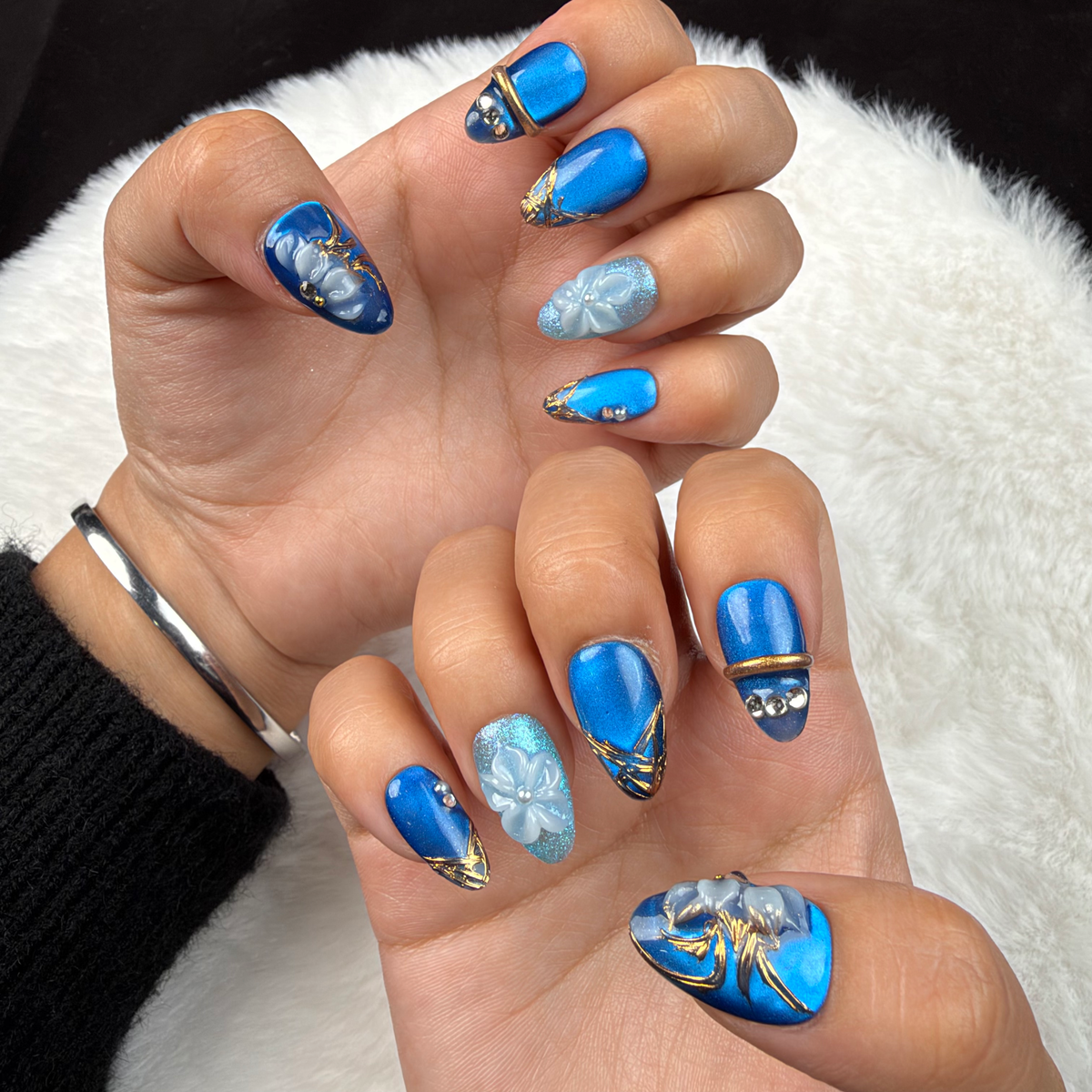 Close-up of hands wearing Blue Orchid cobalt and aqua floral almond press-on nails with gold lines