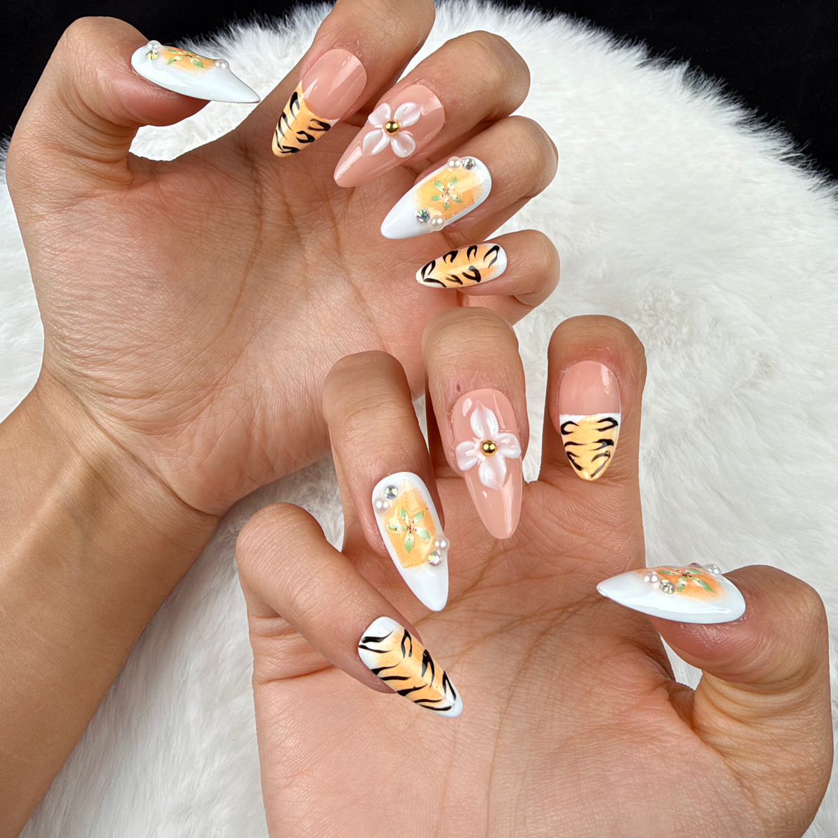 Close-up of hands wearing Tiger Lily orange tiger stripe and floral almond press-on nails