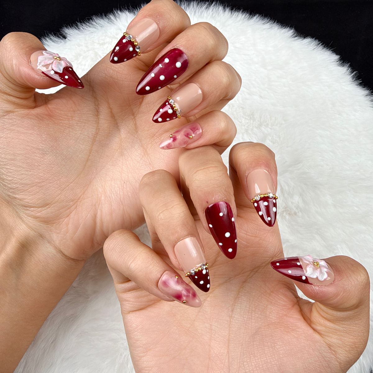 Close-up of hands wearing Cherry Blossom burgundy polka dot French tip floral almond press-on nails