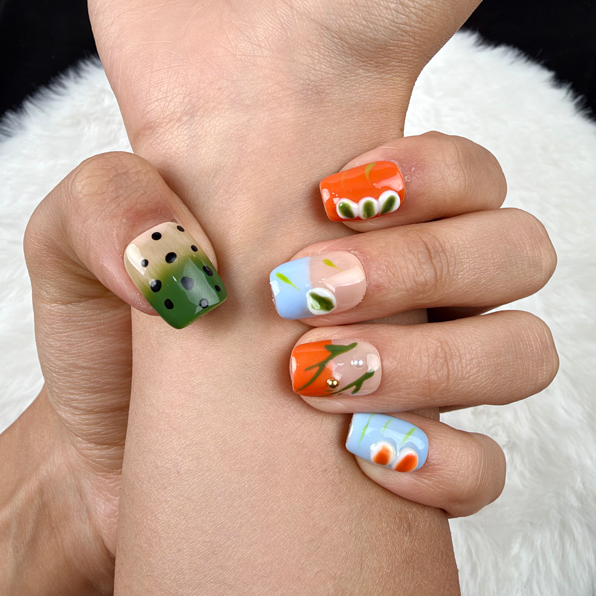 Detail shot of Summer Orchard orange, blue and green floral square press-on nails on hand