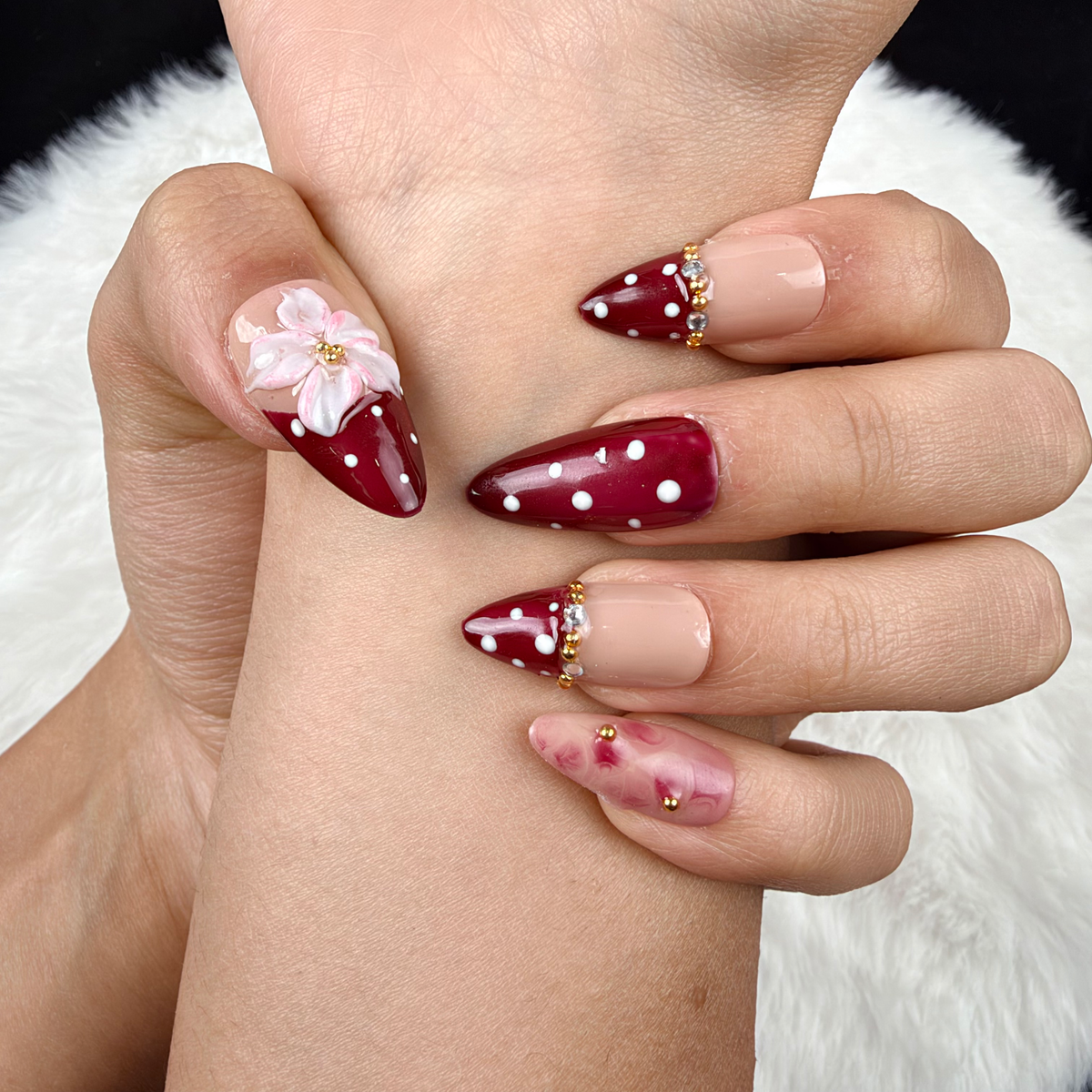 Detail shot of Cherry Blossom burgundy polka dot French tip floral almond press-on nails on hand
