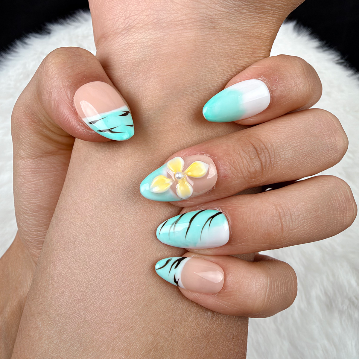 Detail shot of Mint Breeze mint French tip and yellow floral almond press-on nails on hand