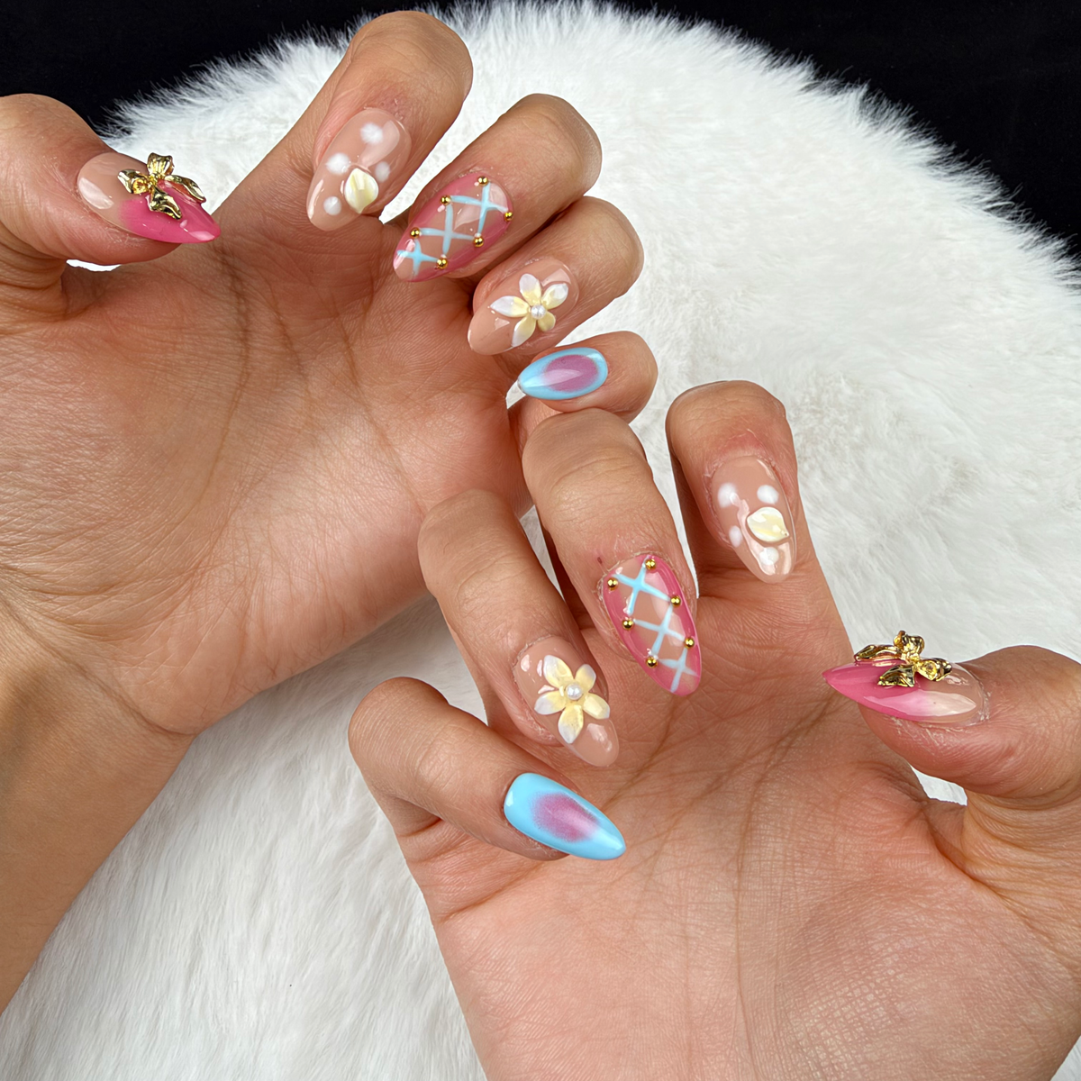 Close-up of hands wearing Sorbet Charms pink, blue and peach floral almond press-on nails with gold charms