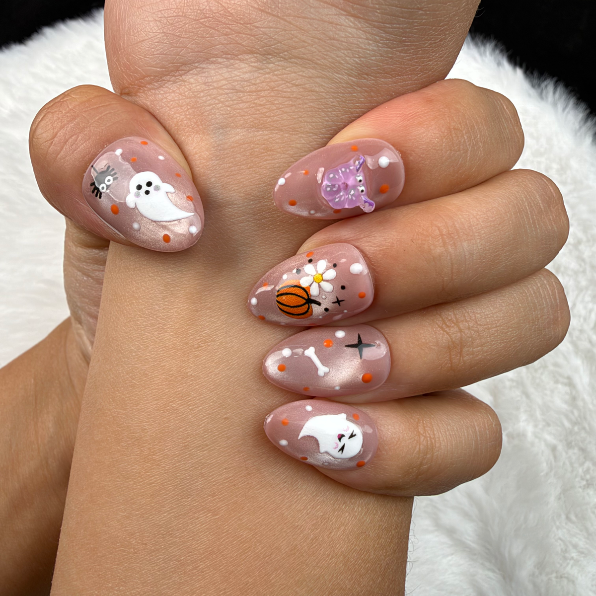 Close-up of hands wearing Pastel Haunt nude almond press-on nails with cute ghost and pumpkin Halloween designs