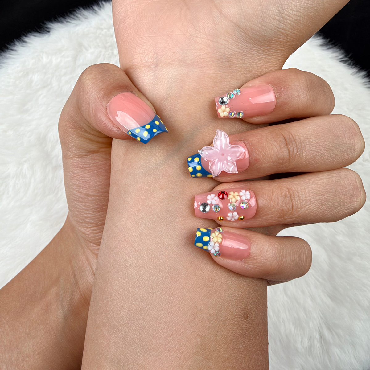 Detail shot of Daisy Confetti blue and pink polka dot French tip floral square press-on nails on hand