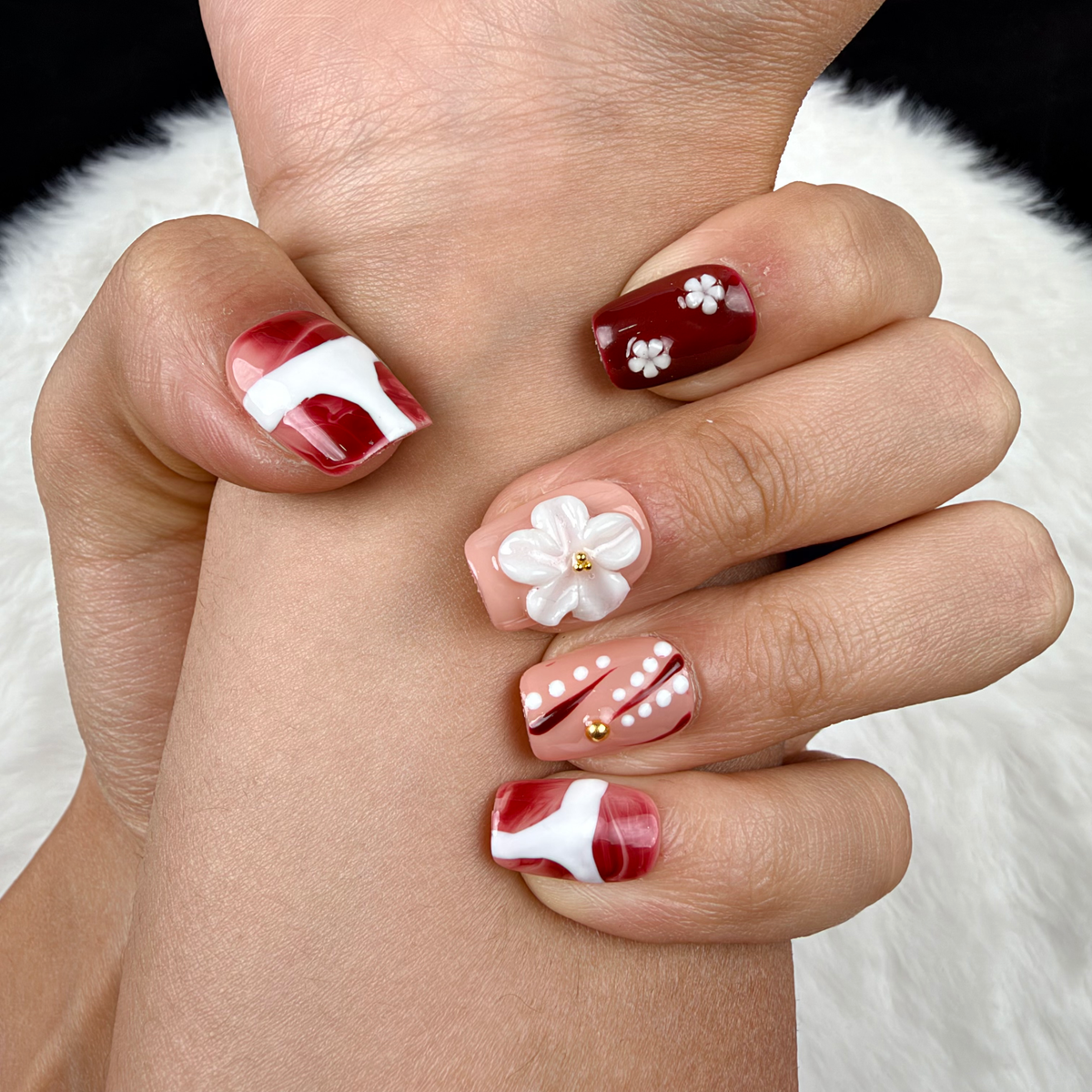 Detail shot of Burgundy Blossom burgundy and nude floral square press-on nails with white flowers on hand