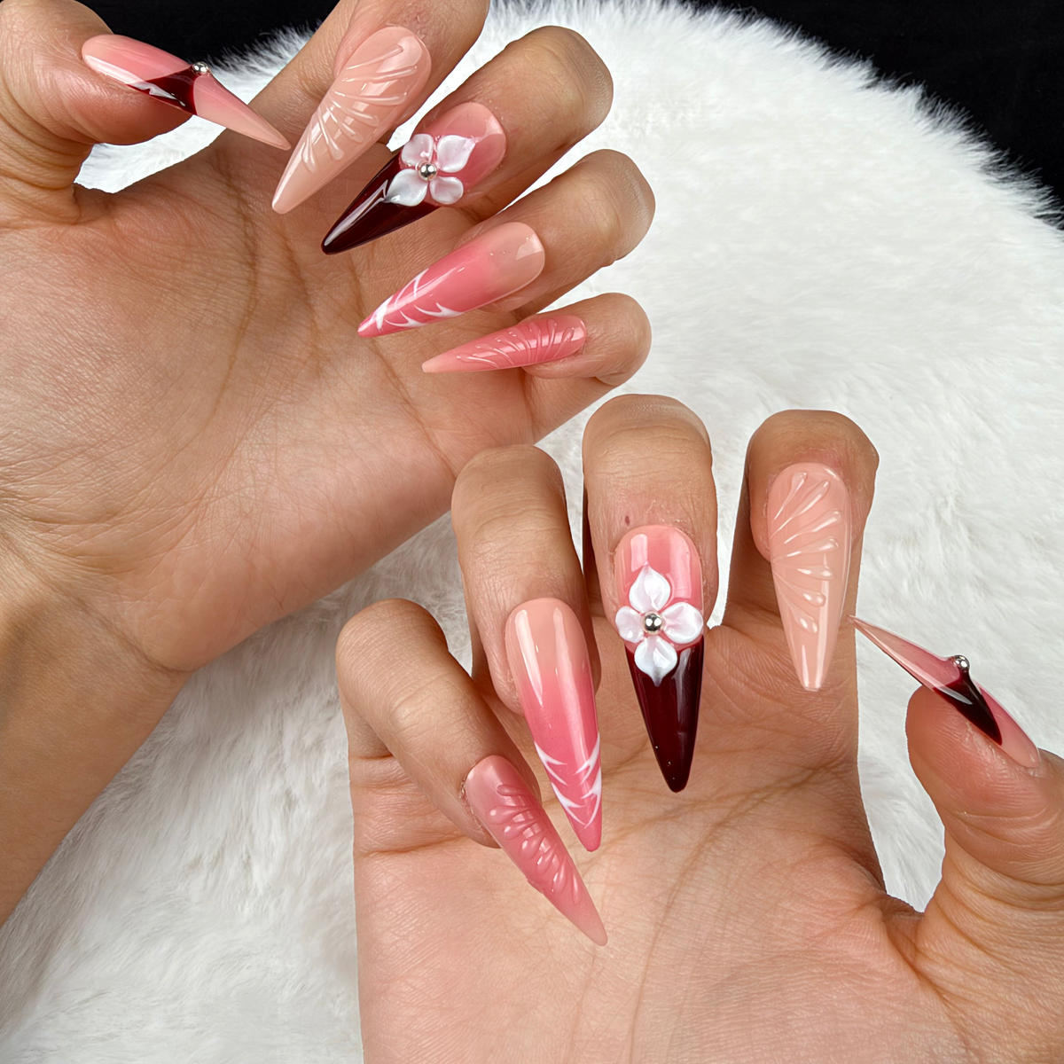 Close-up of hands wearing Crimson Petal red and nude pink floral stiletto press-on nails