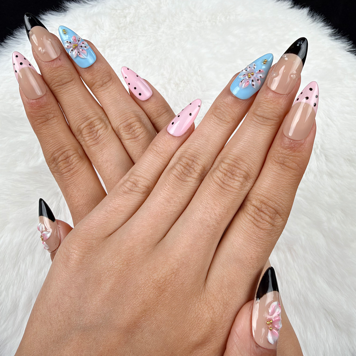 Hands wearing Playful Petals pink, blue and black polka dot floral almond press-on nails