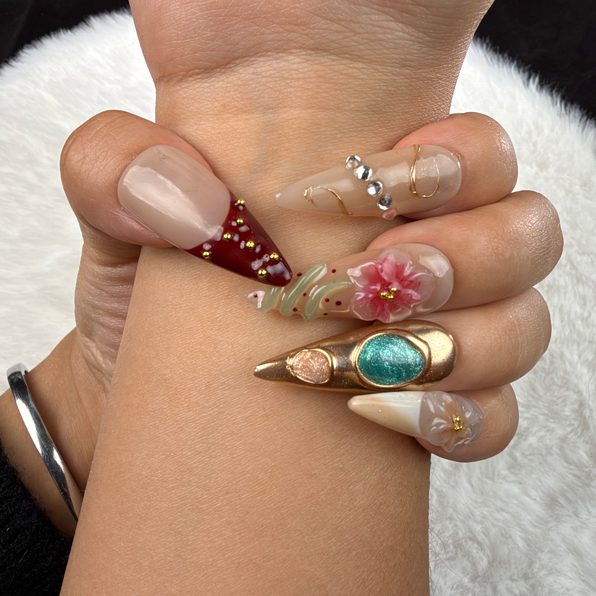 Hands wearing Gilded Garden nude, burgundy and turquoise floral almond press-on nails with gold accents