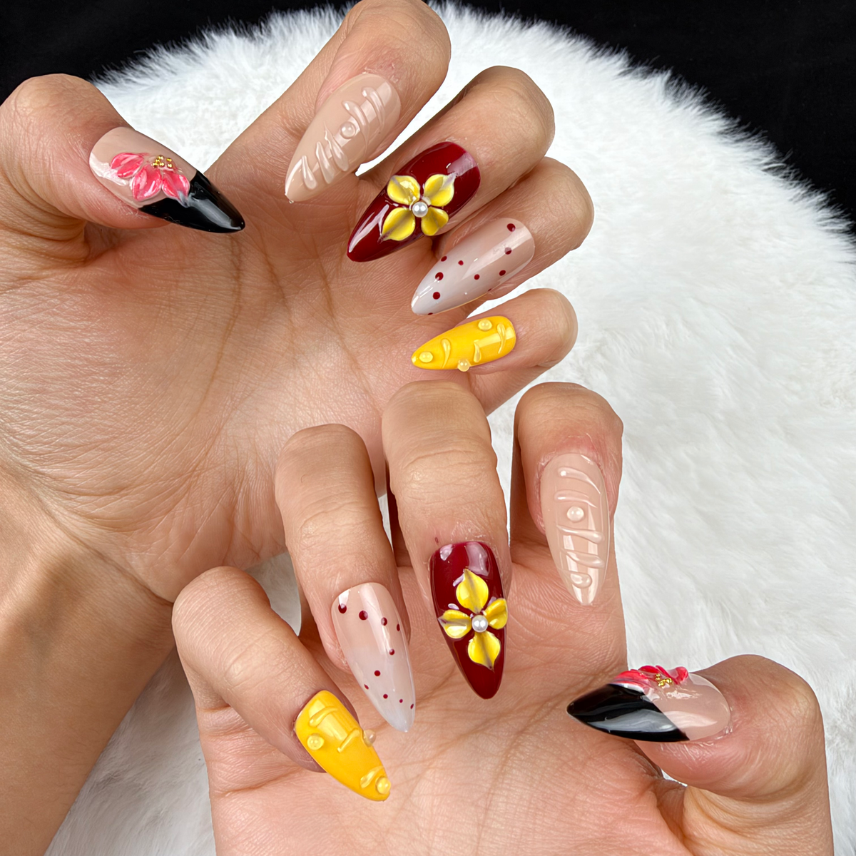Close-up of hands wearing Golden Orchid yellow, burgundy and black floral almond press-on nails