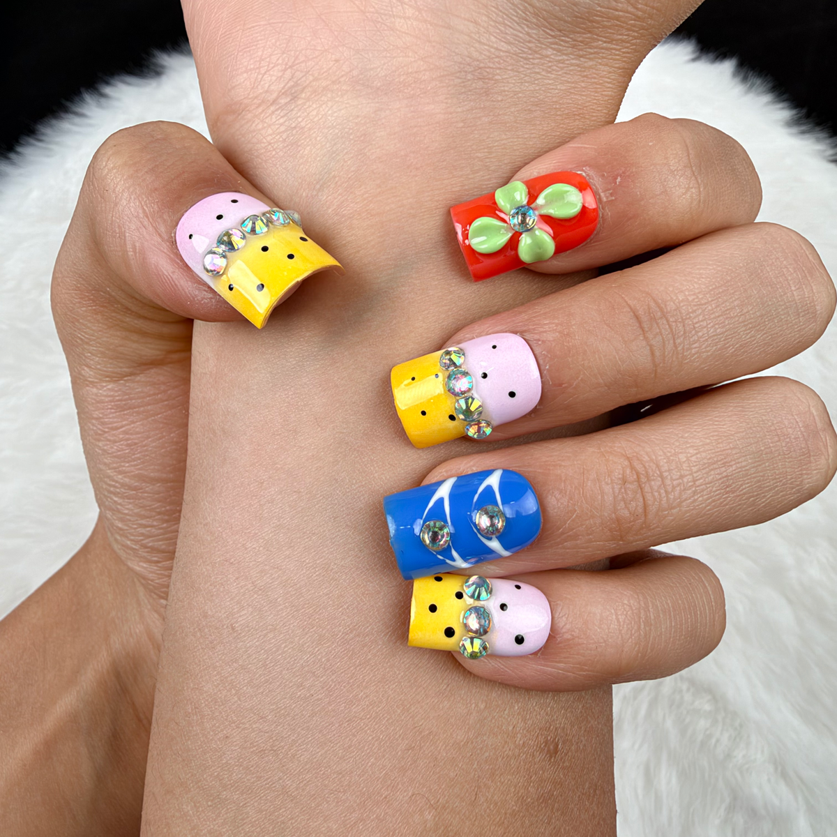 Detail shot of Colour Parade yellow, pink and blue floral square press-on nails on hand