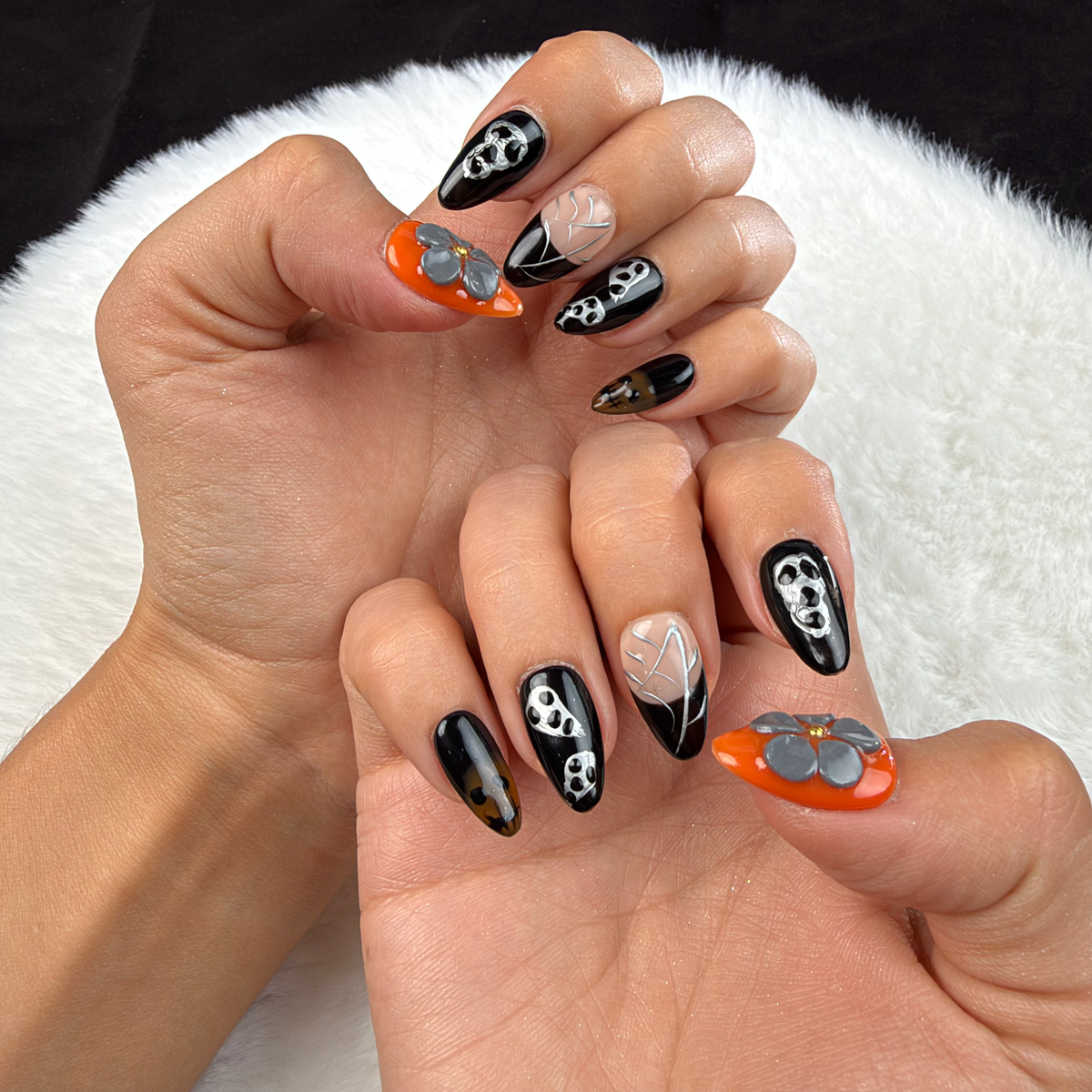 Hands wearing Midnight Web black and orange skull and spiderweb almond press-on nails