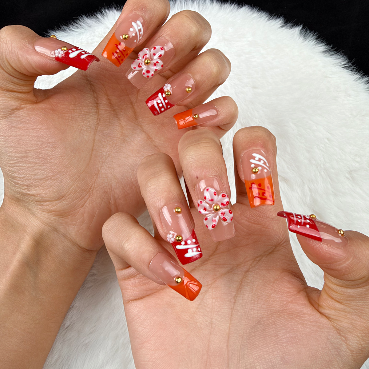 Close-up of hands wearing Coral Ribbon coral and orange floral square press-on nails