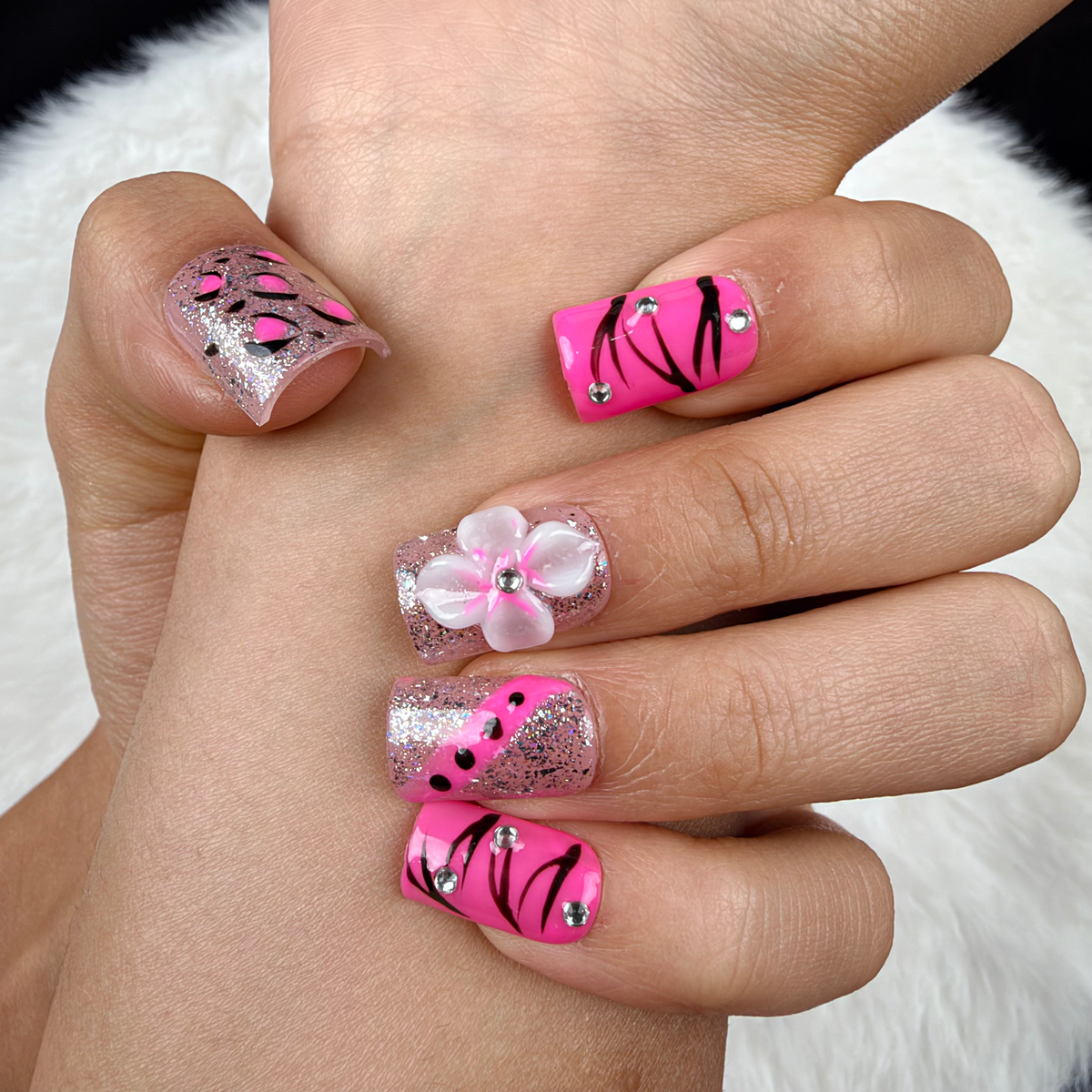 Detail shot of Pink Spark hot pink, black and silver floral square press-on nails on hand