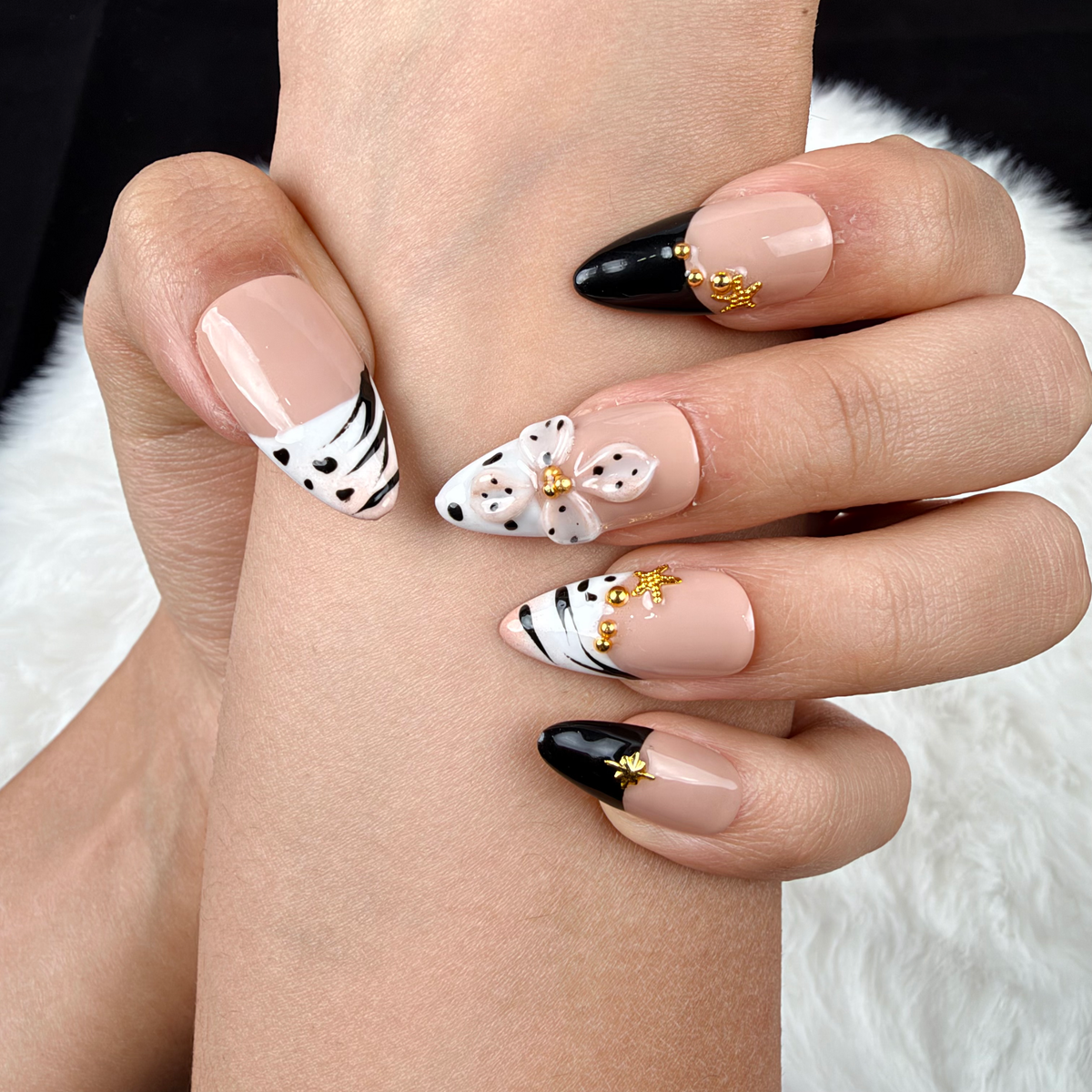 Detail shot of Golden Safari black and white zebra print French tip almond press-on nails with gold accents on hand