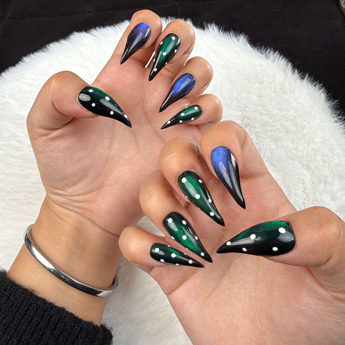 Hands wearing Emerald After Dark green and blue cat eye stiletto press-on nails with rhinestones