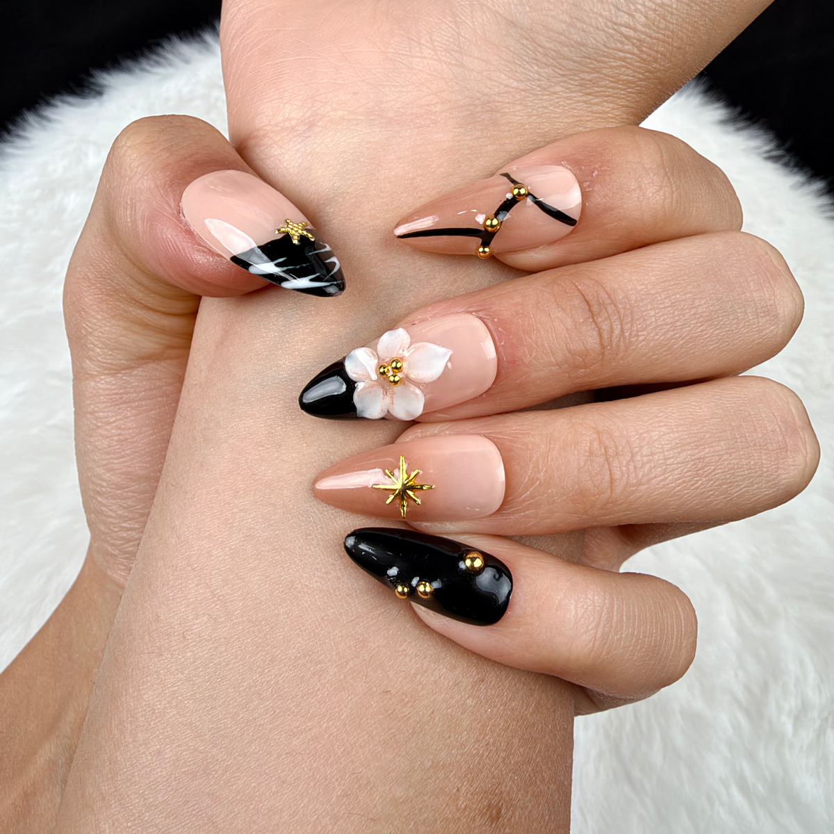 Detail shot of Starry Noir black French tip star and floral almond press-on nails on hand