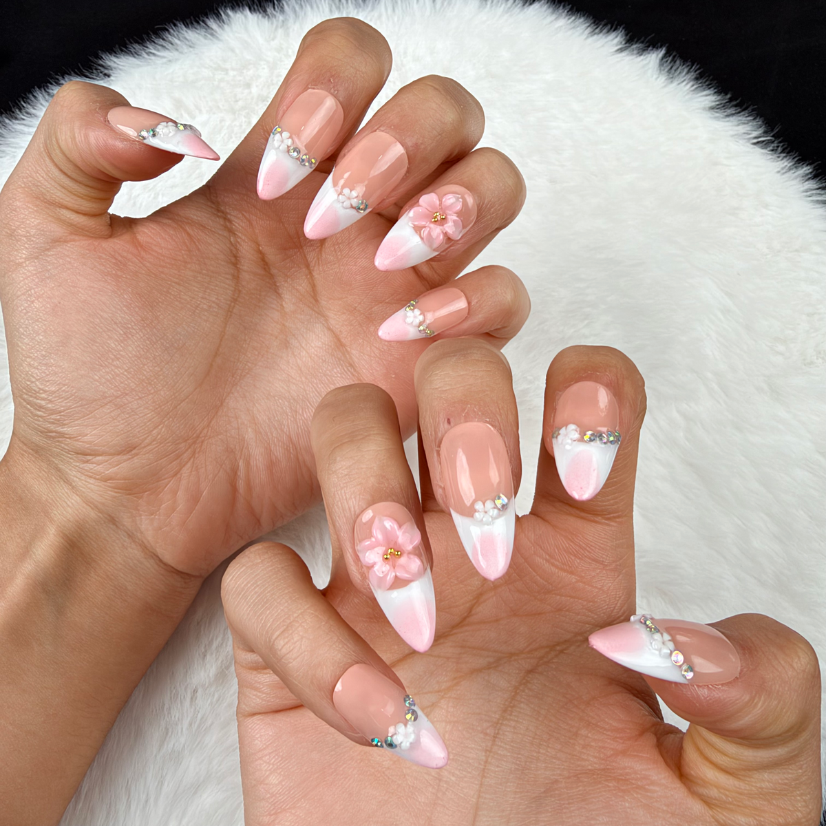 Close-up of hands wearing Blush Tiara pink French tip press-on nails with sparkle and floral accents