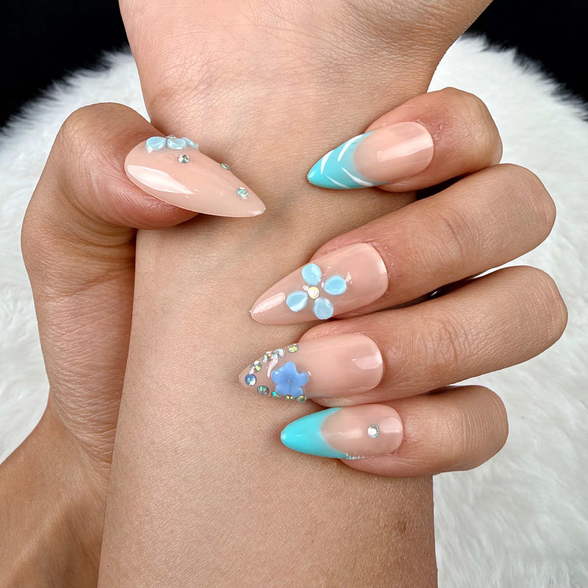 Detail shot of Aqua Blossom turquoise French tip and blue floral almond press-on nails on hand