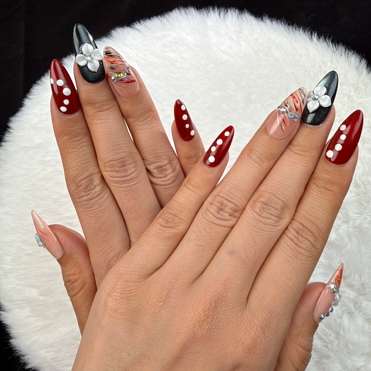 Detail shot of Ruby Petal red and black floral almond press-on nails with rhinestones on hand