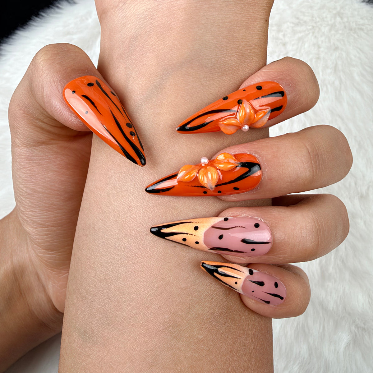 Close-up of hands wearing Tangerine Edge orange chrome and nude pink stiletto press-on nails with black floral details