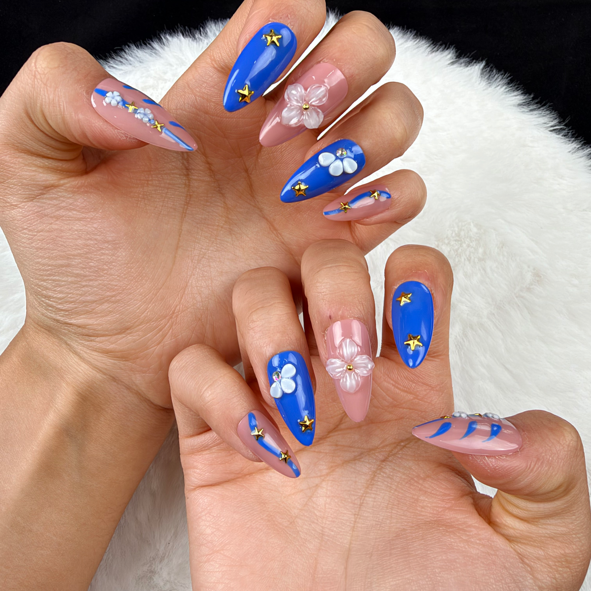 Close-up of hands wearing Blue Starlight cobalt blue and pink floral star almond press-on nails