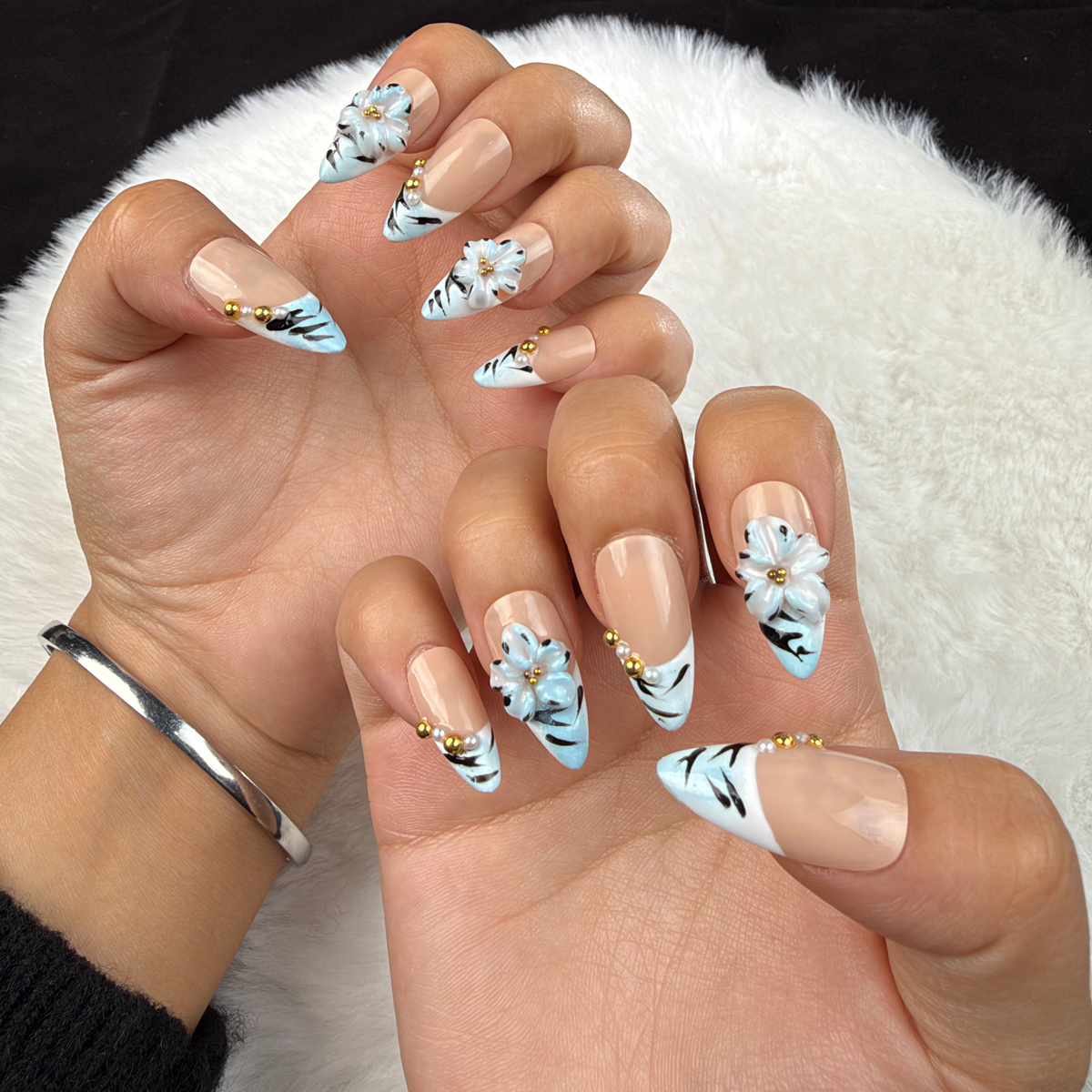 Hands wearing Frost Bloom ice blue striped French tip almond press-on nails with white flowers