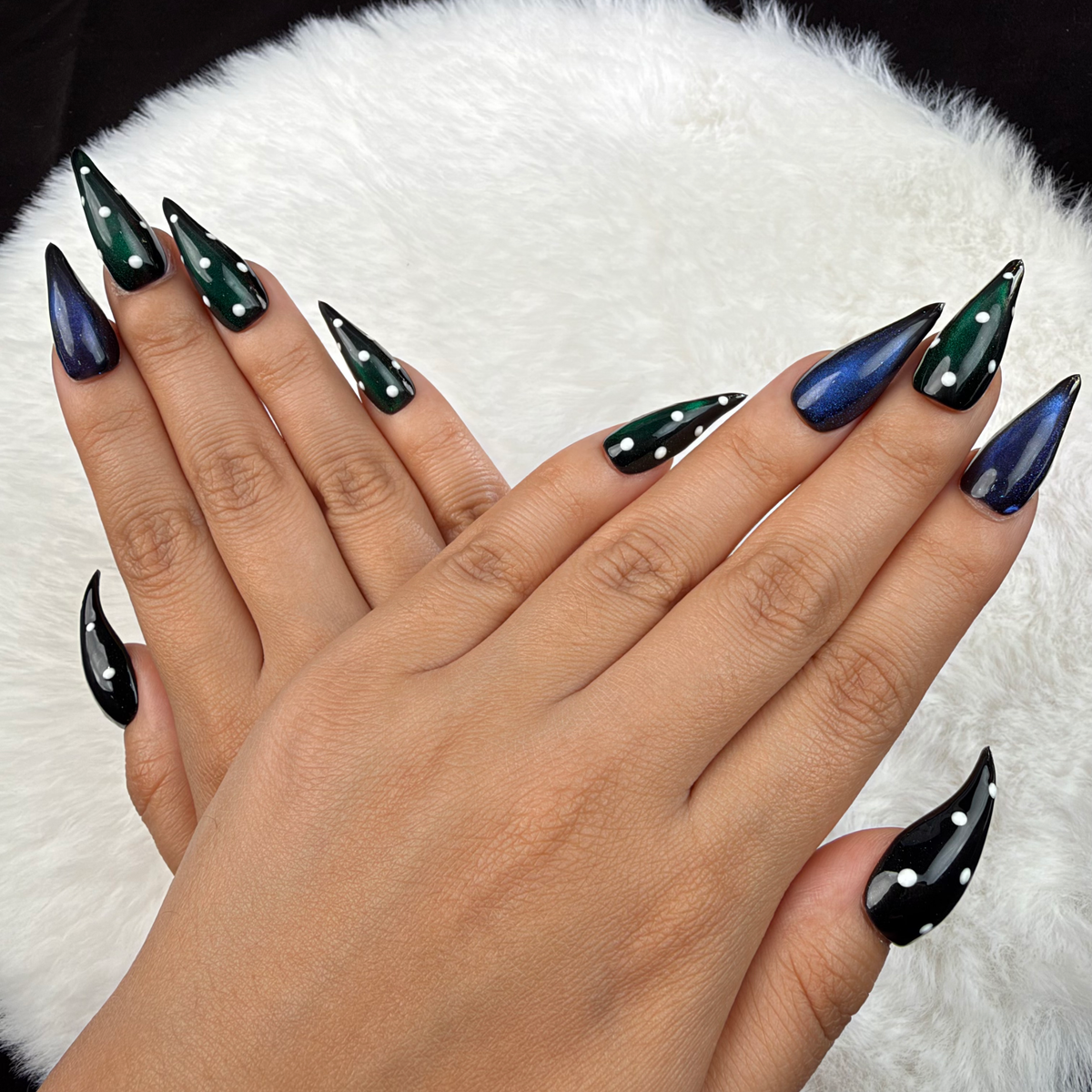 Detail shot of Emerald After Dark green and blue cat eye stiletto press-on nails with rhinestones on hand