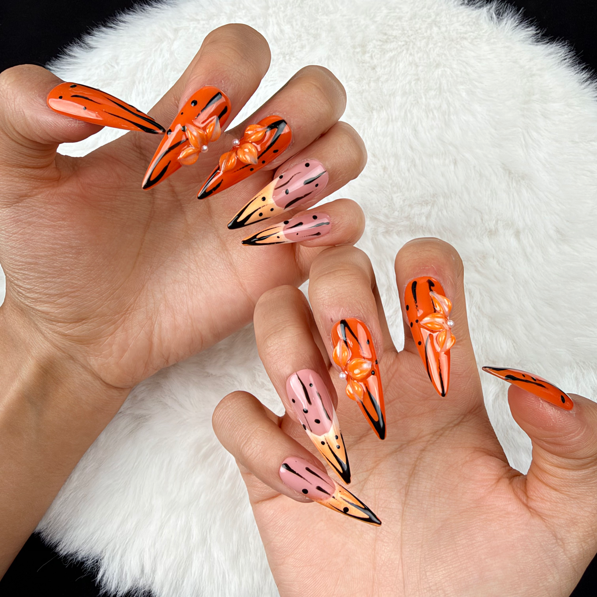Close-up of hands wearing Tangerine Edge orange chrome and nude pink stiletto press-on nails with black floral details