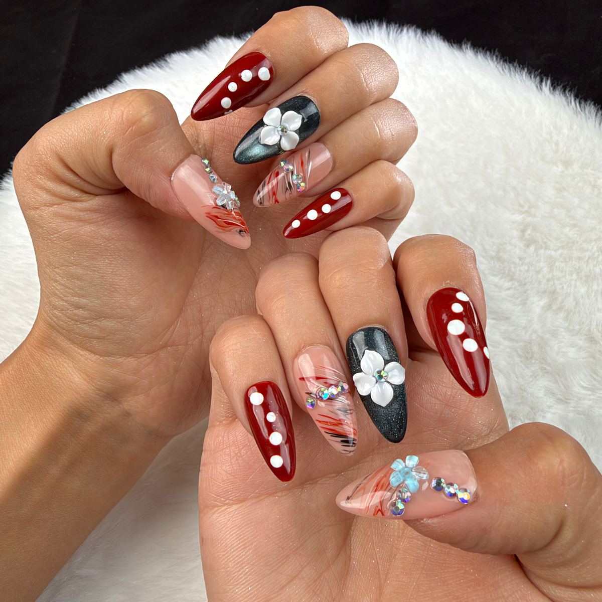 Hands wearing Ruby Petal red and black floral almond press-on nails with rhinestones