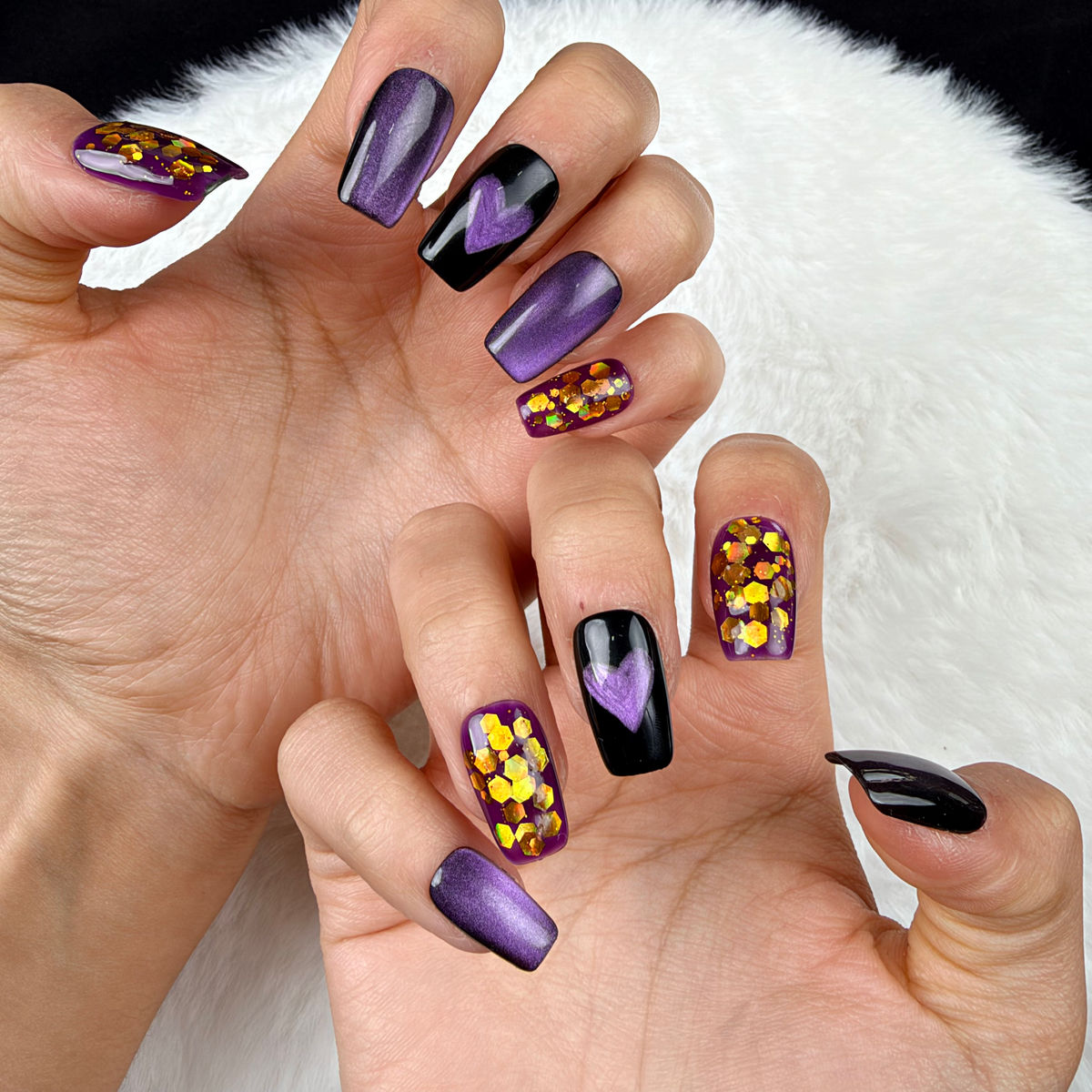Close-up of hands wearing Purple Hearts purple cat eye and gold glitter heart square press-on nails