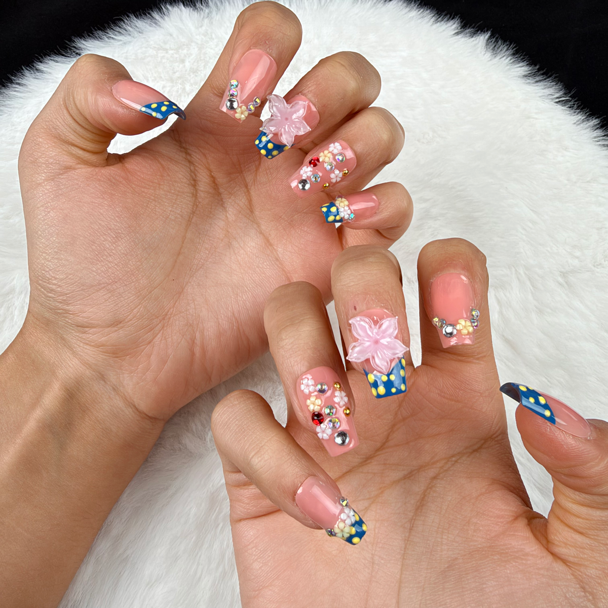 Close-up of hands wearing Daisy Confetti blue and pink polka dot French tip floral square press-on nails
