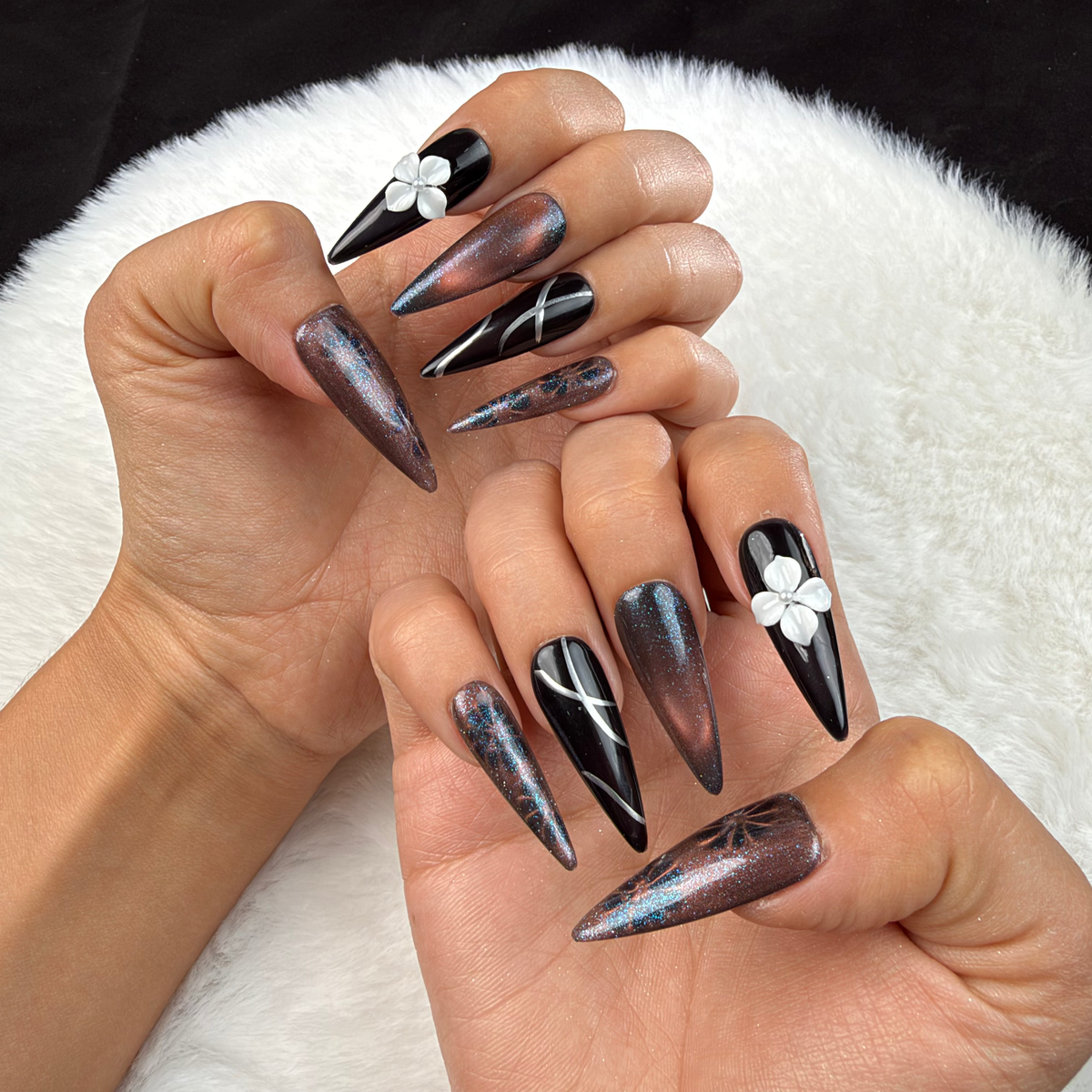 Hands wearing Smoky Bloom black and smoky grey stiletto press-on nails with a white 3D flower