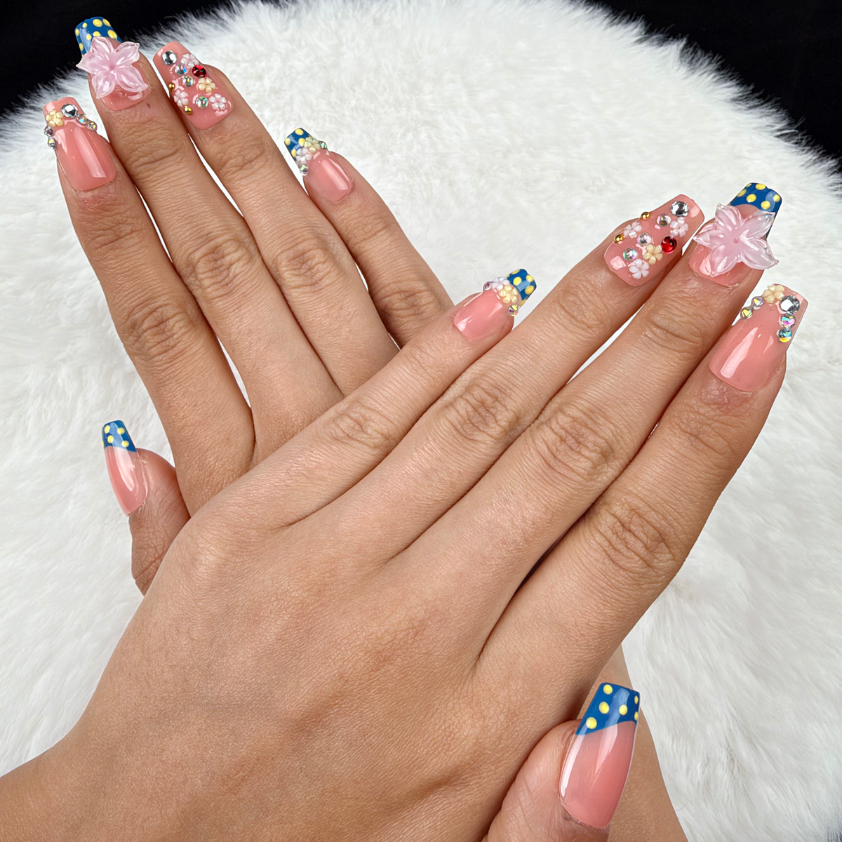 Hands wearing Daisy Confetti blue and pink polka dot French tip floral square press-on nails