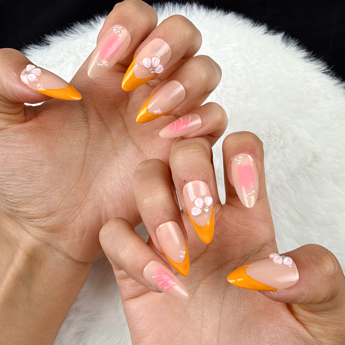Close-up of hands wearing Apricot Petals orange French tip and pink floral almond press-on nails