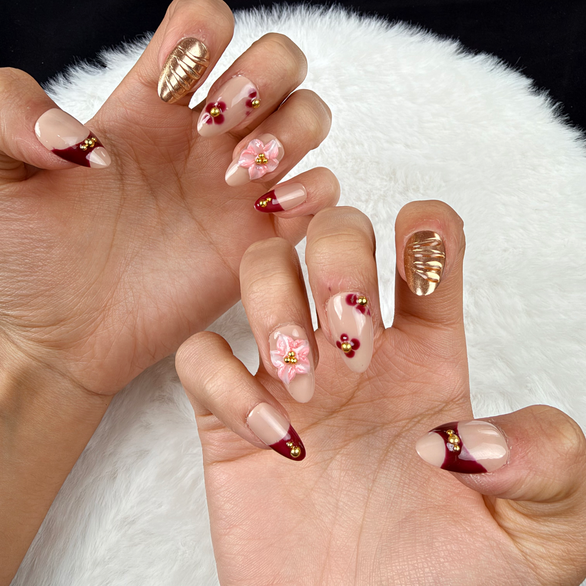 Close-up of hands wearing Amber Rose burgundy, gold-tone and pink floral almond press-on nails